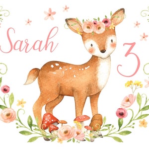 Könnte beinhalten: Eine Aquarell-Illustration eines Rehs, das eine rosa Blumenkrone trägt. Das Reh steht auf einer Wiese mit rosa und gelben Blumen und roten Pilzen. Der Text "Sarah 3" ist in rosa Buchstaben geschrieben.