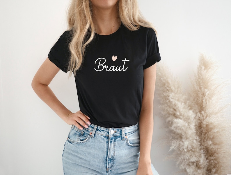 May include: A black t-shirt with the word "Braut" in white cursive lettering and a small pink heart above the word.