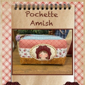 Può includere: Una piccola borsa rettangolare in tessuto patchwork con chiusura a zip. La borsa è decorata con un motivo floreale rosso, bianco e blu e un piccolo viso di ragazza ricamato. La borsa è etichettata "Pochette Amish" e include il testo "Laura Mori, Calle Hibisco 1 Local 55, CC el Campanario, 35660 Corralejo, www.lauramoripatch.com".