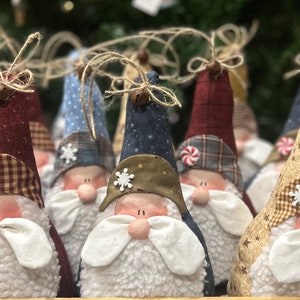 Könnte beinhalten: Eine Gruppe von sechs handgefertigten Gnom-Ornamenten mit verschiedenen farbigen Hüten und gemustertem Stoff. Die Gnome haben weiße Bärte und Gesichter mit bemalten Details.