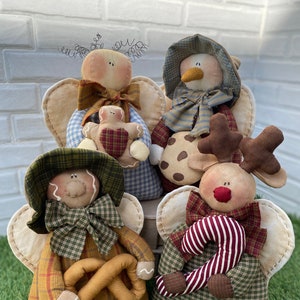 Può includere: Quattro angeli di stoffa fatti a mano con diversi accessori a tema natalizio. Gli angeli sono vestiti in tessuto a quadri e hanno le ali. Un angelo tiene un omino di pan di zenzero, uno tiene un biscotto, uno tiene un pretzel e uno tiene una canna di zucchero.