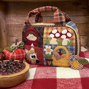 Könnte beinhalten: Eine rote und weiße karierte Stofftasche mit Reißverschluss. Die Tasche hat ein Patchwork-Design mit Applikationen einer Mädchens in einer roten Kapuze, einem Wolf, Pilzen, einer Blume und einem Korb. Die Tasche liegt auf einer rot-weiß karierten Decke.