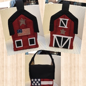 May include: A red and black fabric barn-shaped tote bag with a white star and an American flag on the front. The bag has a black handle and a white star on the back.
