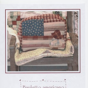 Könnte beinhalten: Eine rote, weiße und blaue gesteppte Tragetasche mit einer kleinen roten, weißen und blauen Puppenfigur auf der Vorderseite. Die Tasche sitzt auf einem Holzstuhl mit einer floral gemusterten Steppdecke.