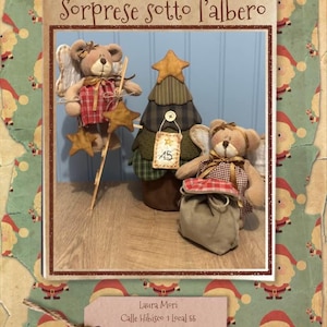 Puede incluir: Una escena navideña decorativa con dos osos de peluche con alas de ángel y un árbol de Navidad de tela. Los osos visten trajes a cuadros y sostienen adornos en forma de estrella. El árbol tiene una estrella y una etiqueta con "15". El texto "Sorprese sotto l'albero" está arriba.