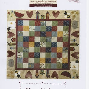 Può includere: Una trapunta beige con un design a patchwork che presenta case, cuori, api e un'anguria. La trapunta è circondata da un bordo marrone e ha il testo "Bless this home" in una cornice marrone.