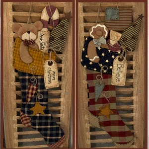 May include: Two Christmas stockings with a patriotic theme. The stocking on the left features a brown teddy bear, a candy cane, a small Christmas tree, and a tag that says "Merry Christmas". The stocking on the right features a gingerbread man, a small Christmas tree, and a tag that says "Believe".