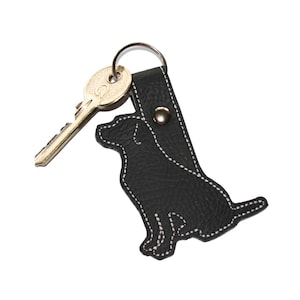 May include: Black leather keychain shaped like a dog, with a silver key ring and a gold key attached.