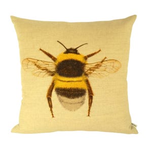 K&ouml;nnte beinhalten: Quadratisches Kissen mit einer detaillierten Illustration einer Hummel. Die Biene hat einen schwarz-gelb gestreiften K&ouml;rper, durchscheinende Fl&uuml;gel und braune Beine. Das Kissen hat einen hellgelben Hintergrund.