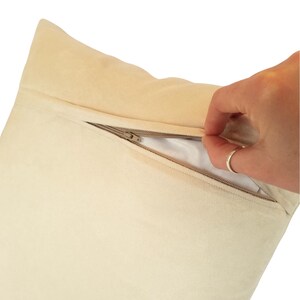 K&ouml;nnte beinhalten: Cremefarbenes Kissen mit verdecktem Rei&szlig;verschluss. Der Rei&szlig;verschluss ist teilweise ge&ouml;ffnet und gibt das wei&szlig;e Innere frei. Das Kissen hat eine weiche, samtige Textur.
