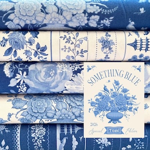 Pode incluir: Uma pilha de rolos de tecido floral azul e branco. O tecido apresenta vários padrões florais, incluindo rosas e outras flores. Um cartão com o texto "SOMETHING BLUE" e uma ilustração floral é visível.