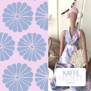 Könnte beinhalten: Ein rosa-blauer Stoff mit einem sich wiederholenden Muster aus stilisierten Blumen. Der Stoff wird neben einer Puppe gezeigt, die ein rosa-blaues Kleid mit einer Muschel in der Hand trägt. Die Puppe trägt einen rosa Hut und ein weißes Stirnband. Der Stoff trägt den Text "Kaffee Fassett Collective".