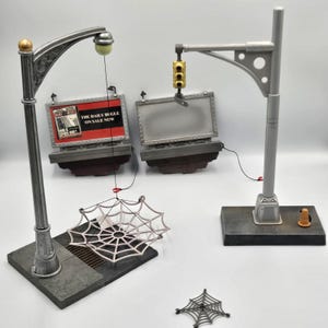 May include: A set of action figure accessories including a silver street lamp with a hanging white web, a grey traffic light pole, two rectangular billboard frames with one displaying The Daily Bugle text, and a small detached black web piece.