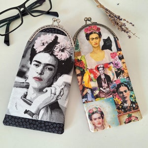 May include: Two Frida Kahlo themed eyeglass cases. One case features a black and white image of Frida Kahlo with a flower crown. The other case features a collage of colourful images of Frida Kahlo.
