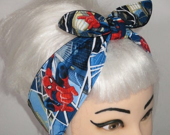 May include: A blue and red Spider-Man patterned headband. The headband features a repeating pattern of Spider-Man in action poses against a cityscape background. The headband is tied in a bow on top of the head.
