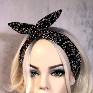 May include: A black and white bandana headband with red accents. The headband is tied in a knot at the top of the head. The headband is worn by a mannequin with blonde hair.