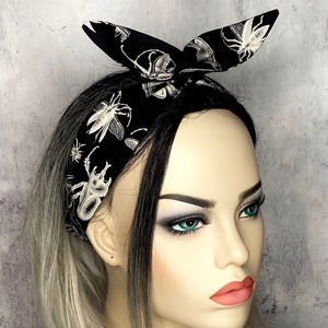 以下が含まれることがあります： 白い昆虫柄の黒いヘッドバンド。ヘッドバンドは、上部にリボン結びされています。