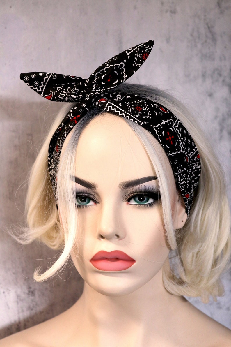 May include: A black and white bandana headband with red accents. The headband is tied in a knot at the top of the head. The headband is worn by a mannequin with blonde hair.