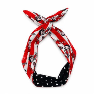 May include: A fabric headband featuring a Betty Boop character print on a red and white striped background, tied in a knot at the top. The reverse side of the headband is black with a white polka dot pattern, creating a reversible design.