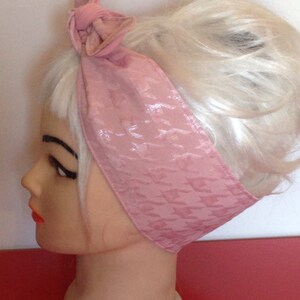 May include: A pink satin headband with a houndstooth pattern. The headband is tied in a bow at the top of the head.