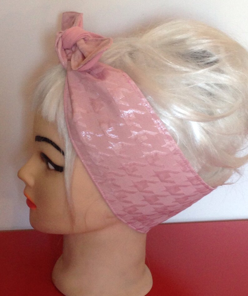 May include: A pink satin headband with a houndstooth pattern. The headband is tied in a bow at the top of the head.