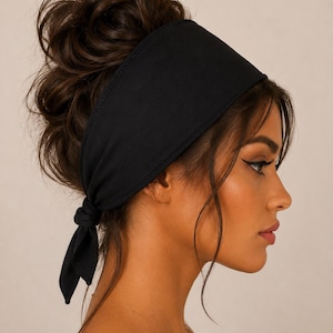 Könnte beinhalten: Ein einfarbiges schwarzes Stoffstirnband mit breitem Design, das sich nach hinten verjüngt, wo es mit einem einfachen Knoten befestigt ist. Das Accessoire liegt über dem Oberkopf, ruht oberhalb der Ohren und ist im Nacken verknotet.