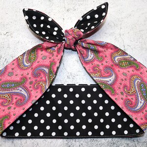 May include: Reversible headband with a pink paisley design and a black and white polka dot pattern. The headband is tied at the top, with two pointed ends. The contrasting patterns are clearly visible.
