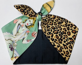 May include: A unique bandana featuring a black base with a green and leopard print design. The green section displays a vintage illustration of a zombie woman. The bandana is tied at the top with a knot and bow.