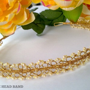 Könnte beinhalten: Ein goldfarbenes Draht-Haarband mit weißen Perlen, die in das Design eingearbeitet sind. Das Haarband liegt auf einer weißen Oberfläche. "KELLY GRACE HEAD BAND" steht unter dem Haarband.