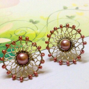 May include: A pair of earrings with a delicate wire design and a pink pearl in the center. The earrings are made of silver wire and have a rose gold finish.