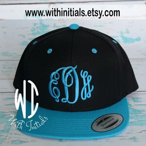 May include: A black and turquoise blue baseball cap with a white embroidered monogram "DDS" on the front. The cap has a snap closure and a "The Classics" Snapback label on the back.