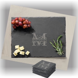 Puede incluir: Una tabla de servir de pizarra negra con una inicial "M" monograma y el nombre "Masterson" grabado en una escritura decorativa. La tabla est&aacute; rodeada de uvas, cubos de queso y ramitas de romero.