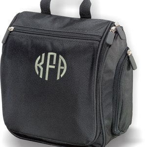 May include: Black travel toiletry bag with a zippered pocket and a monogrammed initial "KFA" in a light gray color.