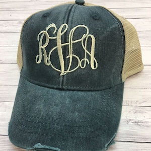 May include: A dark green and tan distressed trucker hat with a white monogram of the letters "RFA" embroidered on the front.