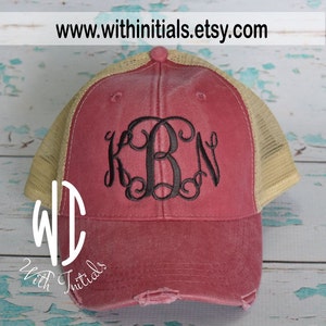 May include: A red and beige distressed trucker hat with a black embroidered monogram "KBN".