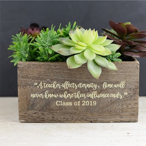 May include: A wooden planter box with a succulent plant arrangement. The box has a quote engraved on it: "A teacher affects eternity. One will never know where their influence ends." The box also has the text "Class of 2019" engraved on it.