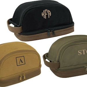 May include: Three toiletry bags with brown leather trim and zipper closures. The bags are black, brown, and green. Each bag has a monogram on the front: KFA, A, and STG.