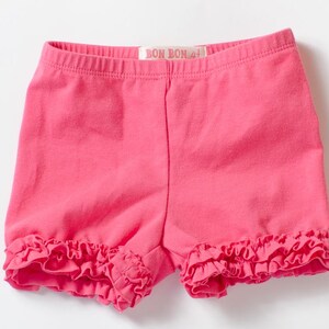 May include: Pink cotton shorts with a ruffled hem and a "Bon Bon" label.