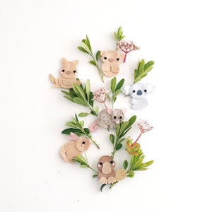 May include: A set of felt animal appliques featuring a koala, a platypus, a kangaroo, a possum, and a koala. The appliques are surrounded by green leaves and pink flowers.