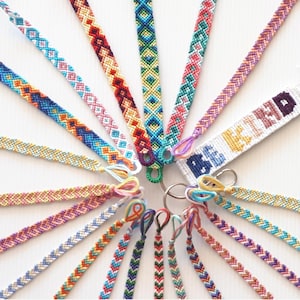 May include: A collection of colourful friendship bracelets with various patterns, including chevron, diamond, and zig-zag designs. The bracelets are arranged in a circle around a key chain with a white friendship bracelet that says "Best Friends".
