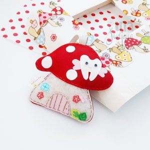 May include: A felt tooth fairy house with a red mushroom roof and white polka dots. The house has a pink door and a white tooth with a smiling face on the mushroom.