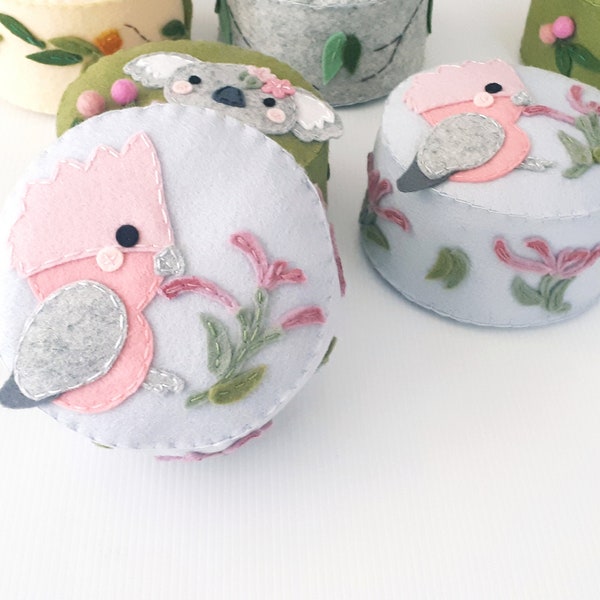 May include: A set of five felt storage boxes with different Australian animal designs. The boxes are round and have a light blue, light green, light yellow, and pink color scheme. The animals include a koala, a bird, and a pink cockatoo.