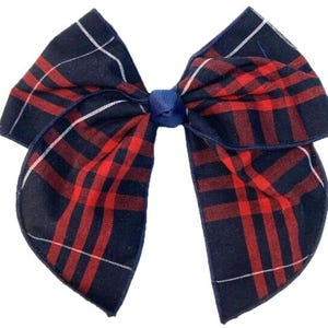 May include: A fabric hair bow featuring a dark navy blue and red plaid pattern with thin white accent lines. The bow is constructed with two large, folded fabric loops on each side, secured in the center by a small, solid navy blue ribbon knot.