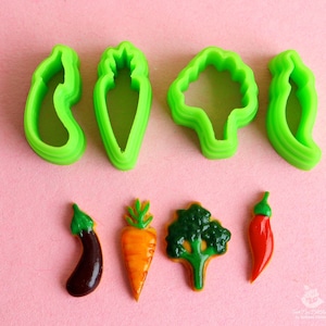 May include: Set of seven green plastic cookie cutters shaped like vegetables, including a carrot, broccoli, eggplant, pepper, and two different shapes of peppers.  The image also shows five decorated cookies shaped like the vegetables.