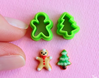 Op de afbeelding: Groene plastic koekjesvormen in de vorm van een gingerbread man en een kerstboom, samen met een gingerbread man en een kerstboomkoekje.