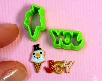 May include: Green plastic cookie cutters shaped like a snowman, an ice cream cone, and the words "YOU" and "JOY".