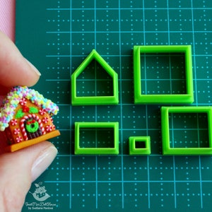 May include: Set of five green plastic cookie cutters shaped like a house, a square, a rectangle, and two smaller squares. The cutters are on a green cutting mat.