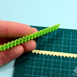 Może przedstawiać: Dwa zielone plastikowe narzędzia z falistym brzegiem. Narzędzia znajdują się na zielonej macie do cięcia z siatką.