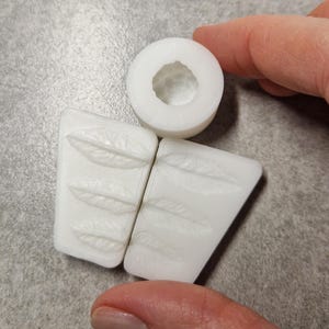 Pu&ograve; includere: Set di stampi bianchi stampati in 3D per la creazione artigianale. Il set include due stampi rettangolari con disegni di piume e uno stampo circolare. Gli stampi sono realizzati in un materiale bianco liscio e solido, perfetti per elementi decorativi.