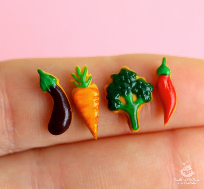 May include: Four miniature food items made of polymer clay: a green eggplant, an orange carrot, a green broccoli, and a red chili pepper.